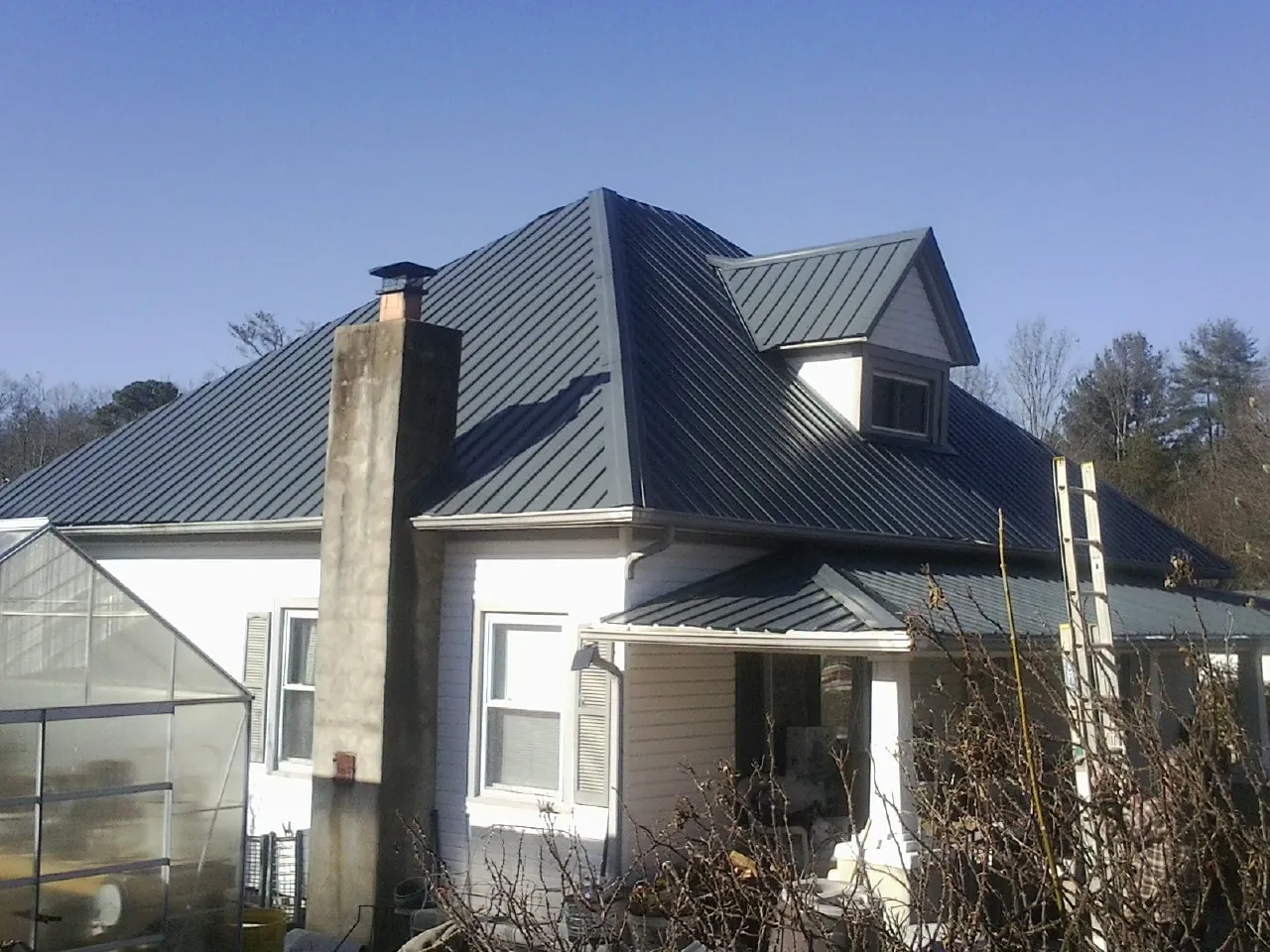Dark blue standing seam metal roof on a white farmhouse with dormer — Slate & Tile Roof Repair by Roofing Brothers in Cottondale