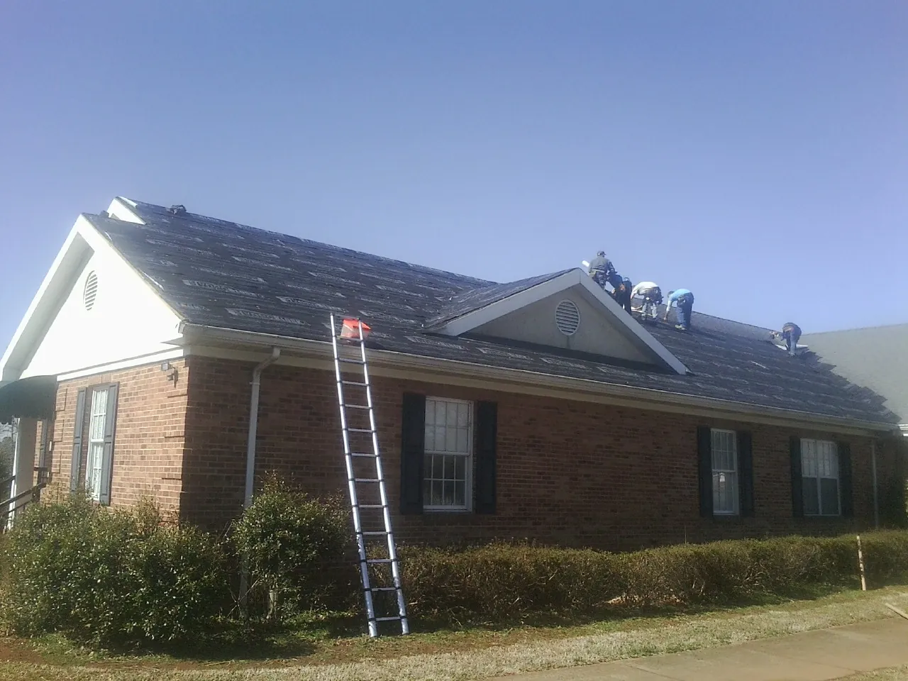 Crew tearing shingles off a brick ranch roof with a ladder set — Emergency Roof Repair work by our crew in Cottondale